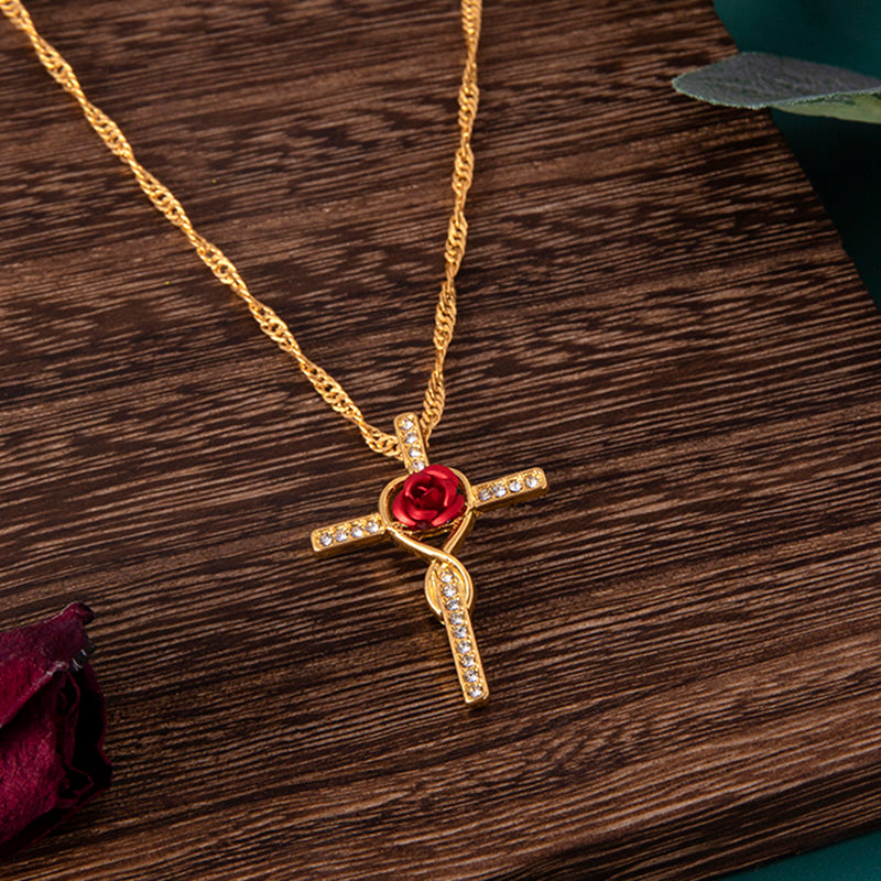 Gold necklace with a red rose and cross pendant on a wooden surface