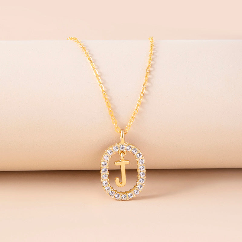 Gold necklace with a pendant featuring the letter 'J' on a beige background