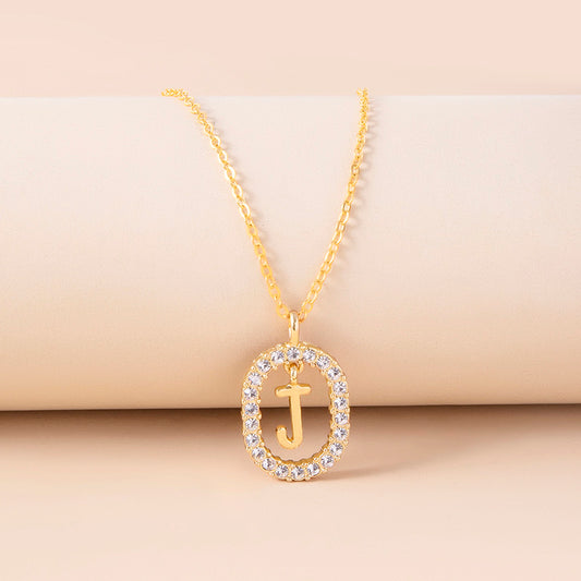 Gold necklace with a pendant featuring the letter 'J' on a beige background