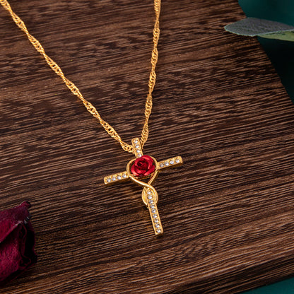Gold necklace with a red rose and cross pendant on a wooden surface