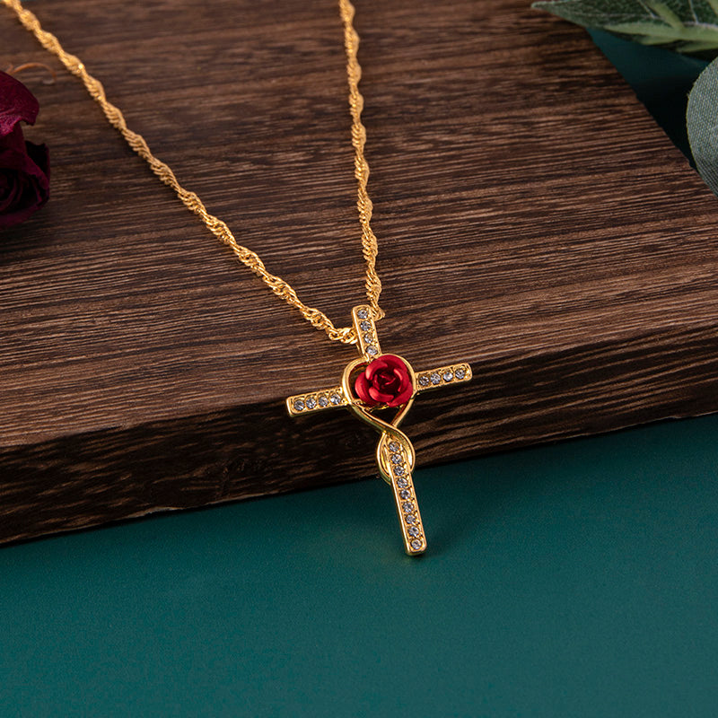 Gold necklace with a red heart and cross pendant on a wooden surface