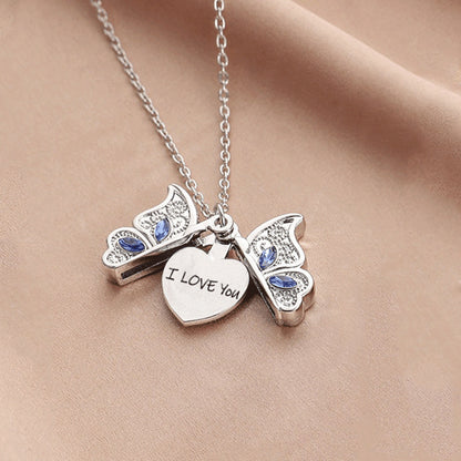 Silver butterfly necklace with 'I LOVE YOU' heart pendant on a beige fabric background